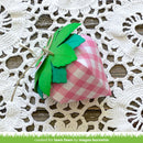 Pink checkered strawberry-shaped box with green leaves on a white lace doily