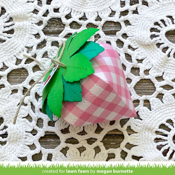 Pink checkered strawberry-shaped box with green leaves on a white lace doily