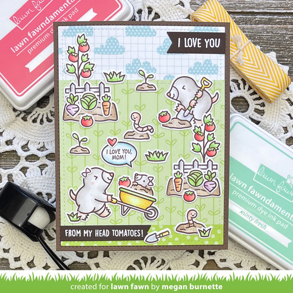 Card with cartoon dog and tomato plants, surrounded by stamping supplies on a wooden surface.