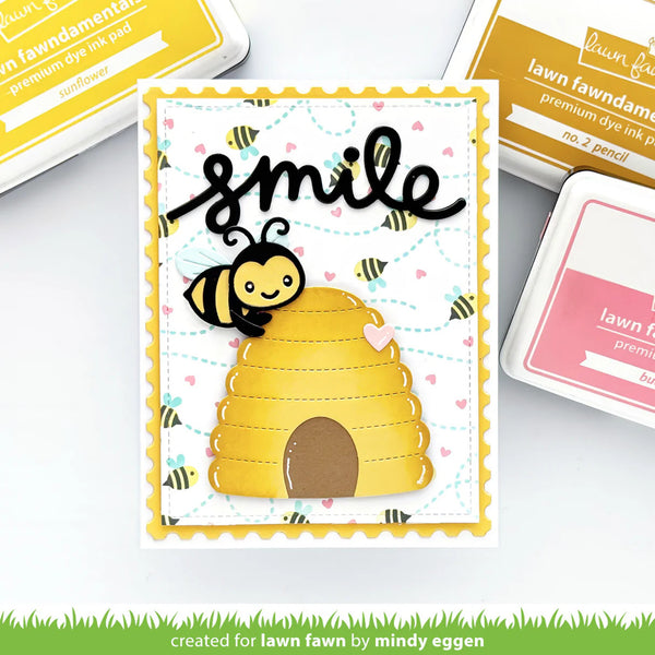 Card with bee and beehive design and 'smile' text, surrounded by ink pads and tools.