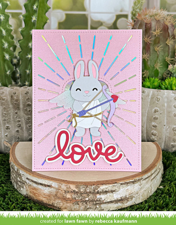 Card with a cartoon bunny holding a bow and arrow on a pink background with 'love' text, placed on a wooden stand with a cactus and succulent plant in the background.