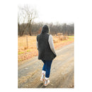 Person wearing a black knit vest and blue jeans walking on a path in a natural setting.
