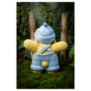 Crocheted character in yellow outfit with blue hat and overalls standing on grass with plants in the background