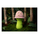 Crocheted mushroom toy with pink cap and green stem in a forest setting