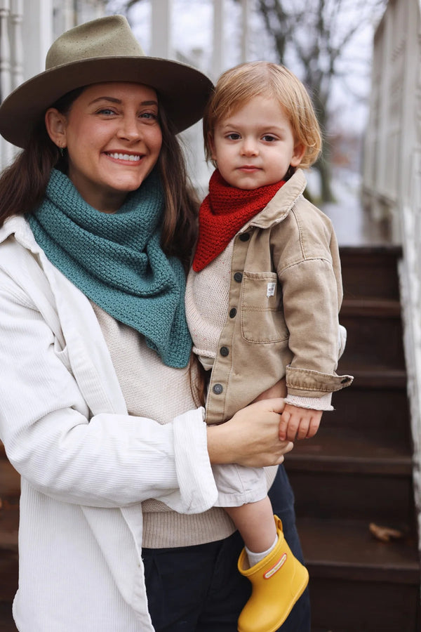 Woman holding a child outdoors, both wearing scarves and coats