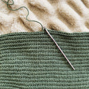 Green knitted fabric with a metal knitting needle on a textured beige surface