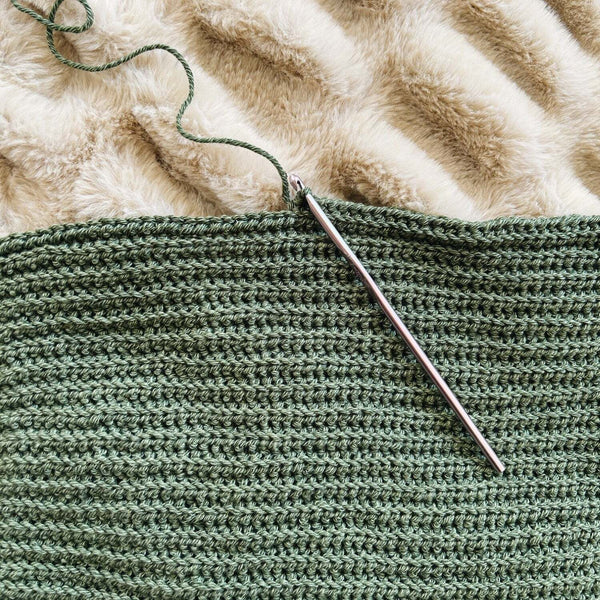Green knitted fabric with a metal knitting needle on a textured beige surface