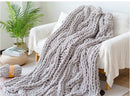 Gray knitted blanket draped over a white sofa in a cozy living room.