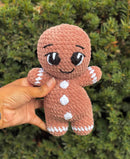 Hand holding a small crochet gingerbread man amigurumi against a green bush background