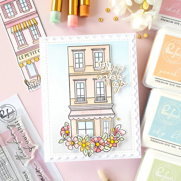 Card with a building illustration and flowers, surrounded by stamping supplies on a pink background