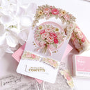 Decorative card with floral design and confetti message, surrounded by flowers and a stamp set.