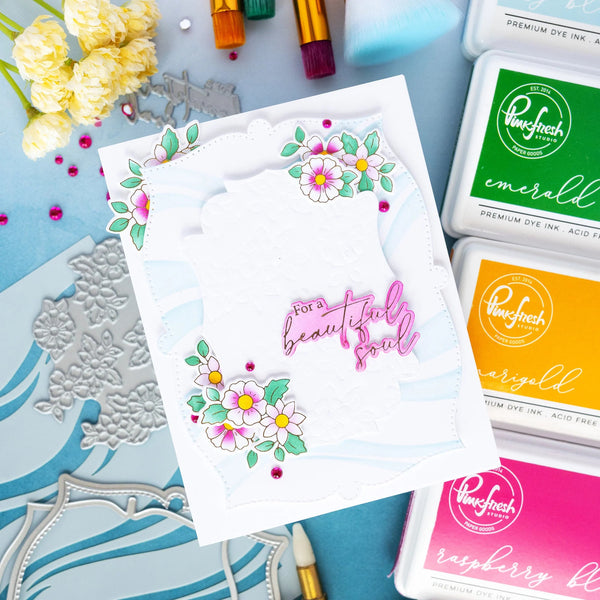 Card with floral design and text 'For a beautiful soul' surrounded by ink pads and stamping tools on a blue surface.