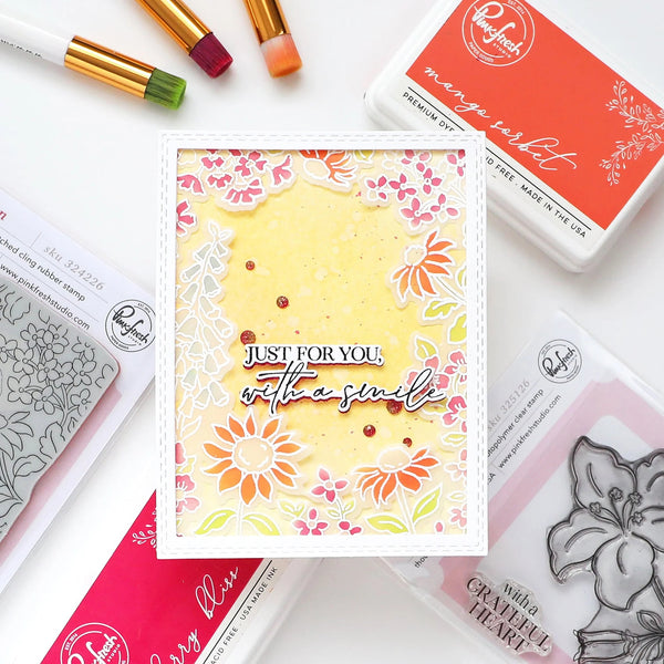 Card with floral design and text 'Just for you, with a smile' surrounded by rubber stamps and ink pads.