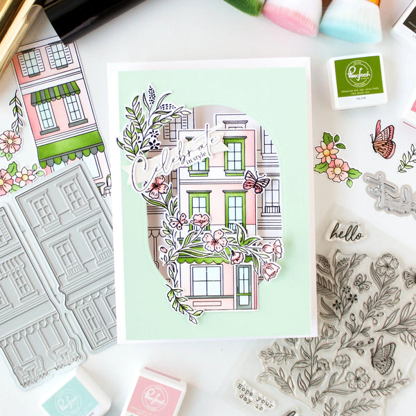 Card with decorative building design and floral elements on a table with stamping tools.