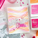 Card with watercolor design and decorative elements on a crafting surface with ink pads and stamps.