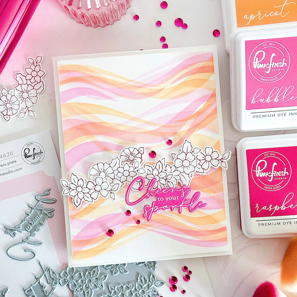 Card with watercolor design and decorative elements on a crafting surface with ink pads and stamps.