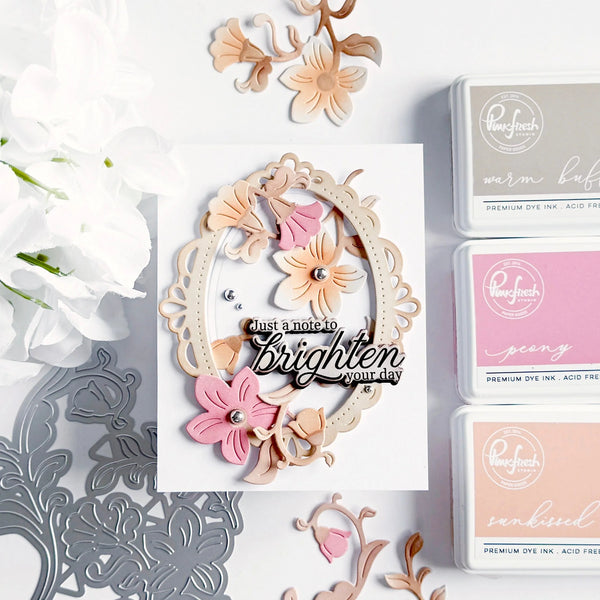Decorative card with floral elements and 'just a note to brighten your day' text, surrounded by craft supplies on a white background.