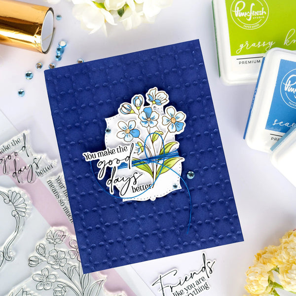 Blue card with floral design and text on a white surface with craft supplies.