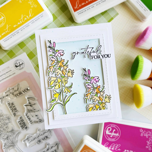 Card with floral design and 'grateful FOR YOU' text, surrounded by stamp pads and tools on a checkered surface.