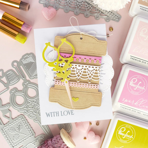 Card with decorative elements on a pink background with stamping supplies.