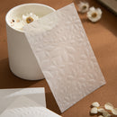 White embossed card with floral design on a brown surface