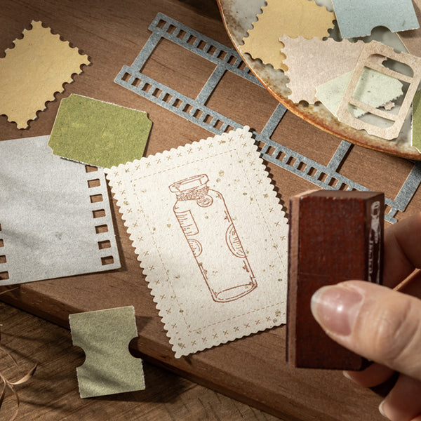 Hand holding a stamp over paper with embossed design on a wooden surface with craft materials.