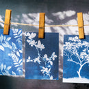Three blue cards with white floral designs hanging on a string with wooden clips against a gray background.