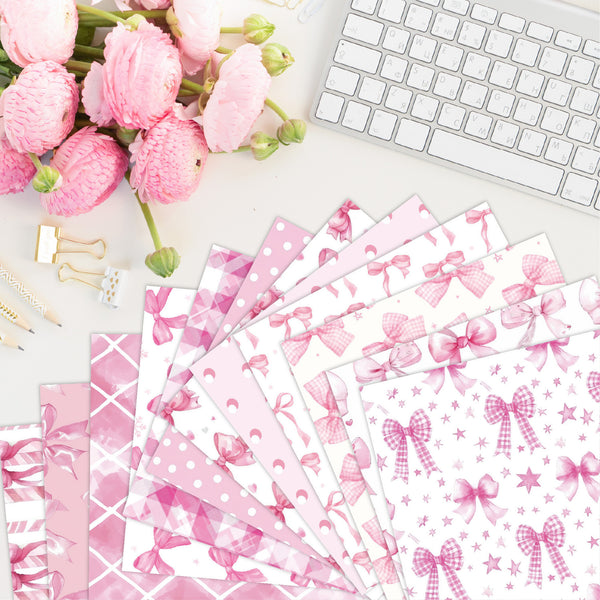 Pink stationery items with bow designs on a desk with flowers and a keyboard.