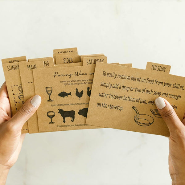 Hands holding brown paper cards with text and illustrations on a light background