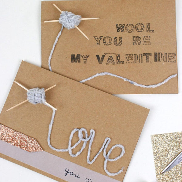 Two brown paper cards with yarn and knitting needles, one saying 'Wool you be my Valentine' and the other 'Love you &', on a white background.