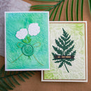 Two handmade cards with floral and leaf designs on a brown surface with greenery.
