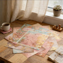 Colorful paper sheets on a wooden table with a cup of coffee and a plant in the background.