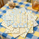 Collection of fabric swatches with bee and check patterns on a checkered tablecloth.