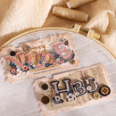 Embroidery hoop with 'Niece' and 'HBD' text and decorative elements on a beige fabric background.