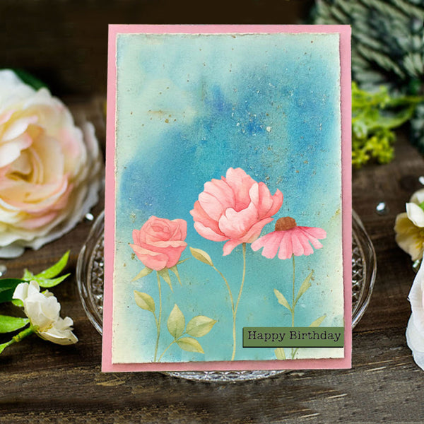 Handmade birthday card with pink flowers and 'Happy Birthday' text on a wooden surface with floral decorations.