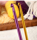Two metallic crochet hooks, one purple and one gold, in front of yarn balls.