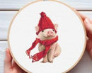 Cross-stitched design of a pig wearing a red hat and scarf on a white background.