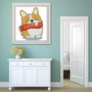 Framed cross-stitched picture of a dog with a red scarf on a light blue wall above a white cabinet.