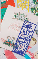 Colorful Christmas cards with a blue cut-out design of mushrooms and leaves.