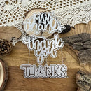 Decorative cutout letters spelling 'Thank you' on a wooden surface with a lace doily and pinecones.
