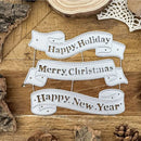 Decorative paper banners with 'Happy Holiday', 'Merry Christmas', and 'Happy New Year' text on a wooden surface.