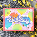 Colorful birthday card with balloons and 'Happy Birthday' text on a textured surface with yellow flowers.