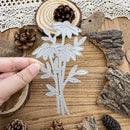 Hand holding a floral metal cutting die on a wooden surface with natural elements.