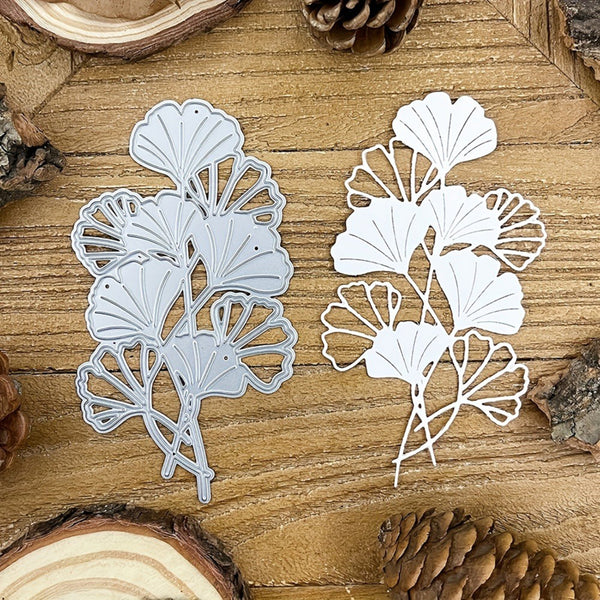 Two white leaf-shaped metal cutting dies on a wooden surface with pine cones.