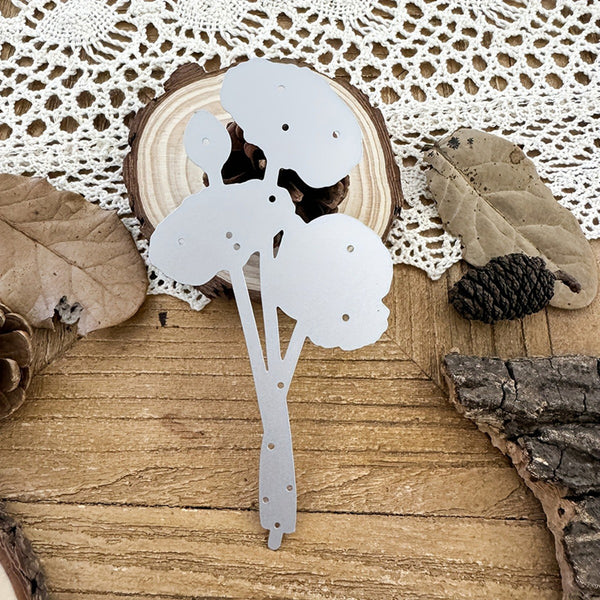 Decorative metal flower on a wooden surface with leaves and pinecones