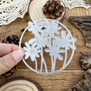 Metal floral cutting die held over a wooden surface with decorative elements.