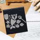 Set of metal stamps with sea-themed designs on a black card, placed on a wooden surface.