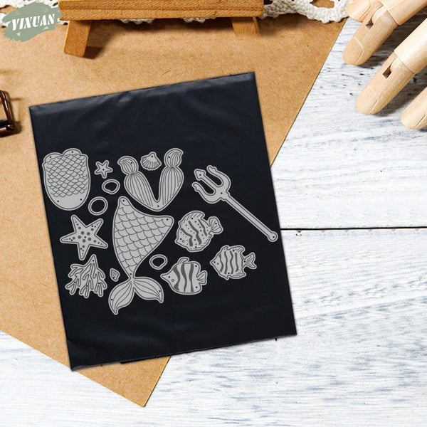 Set of metal stamps with sea-themed designs on a black card, placed on a wooden surface.