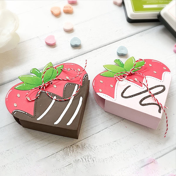 Two strawberry-shaped chocolate boxes on a white surface with colorful candies around.