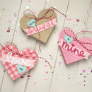 Heart-shaped gift tags with romantic phrases on a wooden surface.